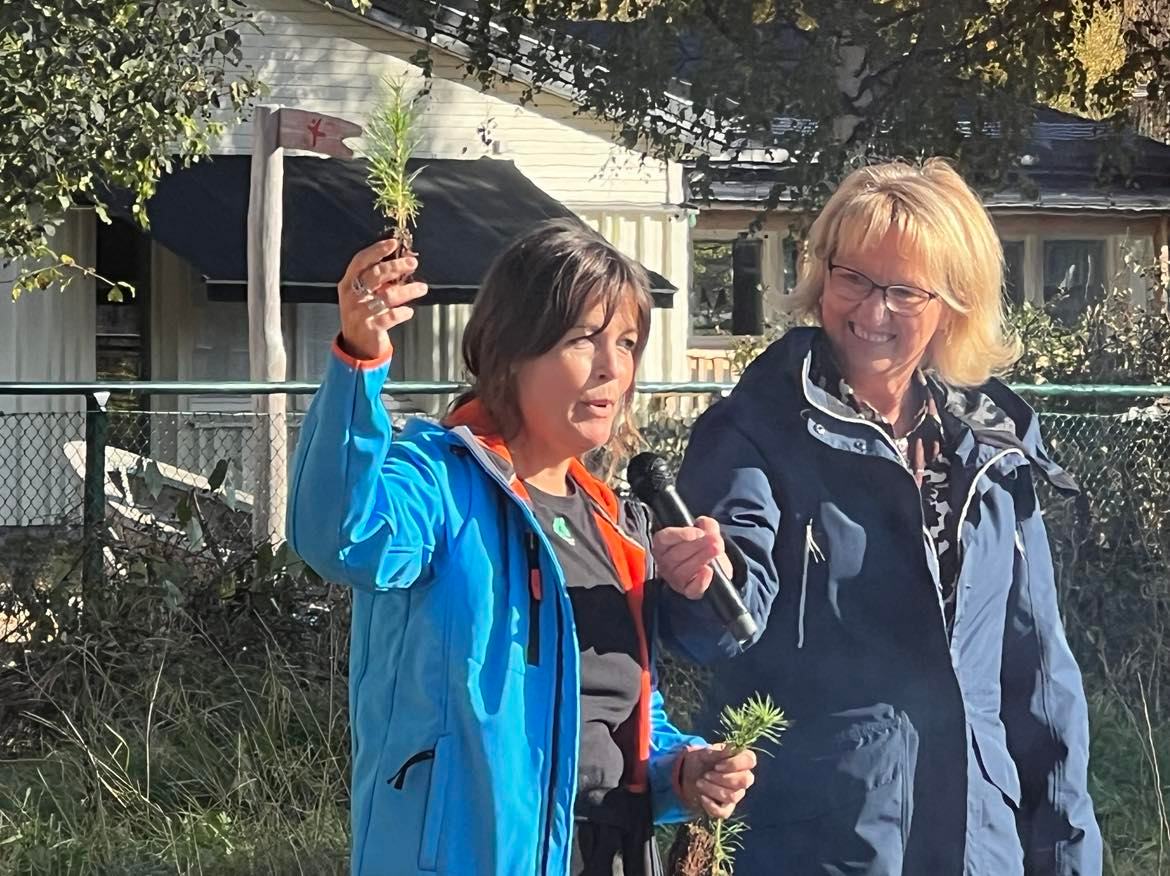 Ewa-Marie Zetterkvist och Lena Heikka står bredvid varandra, Ewa-Marie håller upp en växt och pratar i en mikrofon som Lena håller.