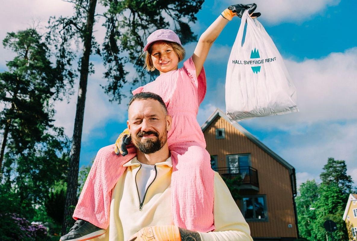 Ett barn i rosa kläder sitter på en mans axlar och håller i en påse med skräp.