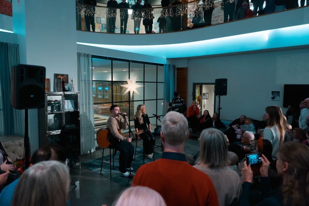 Joel Nordenberg och Monou Nilsson framför en duett på scenen i Strands galleria. Det hänger en julstjärna på en glasvägg bakom dem. Många människor är i publiken.