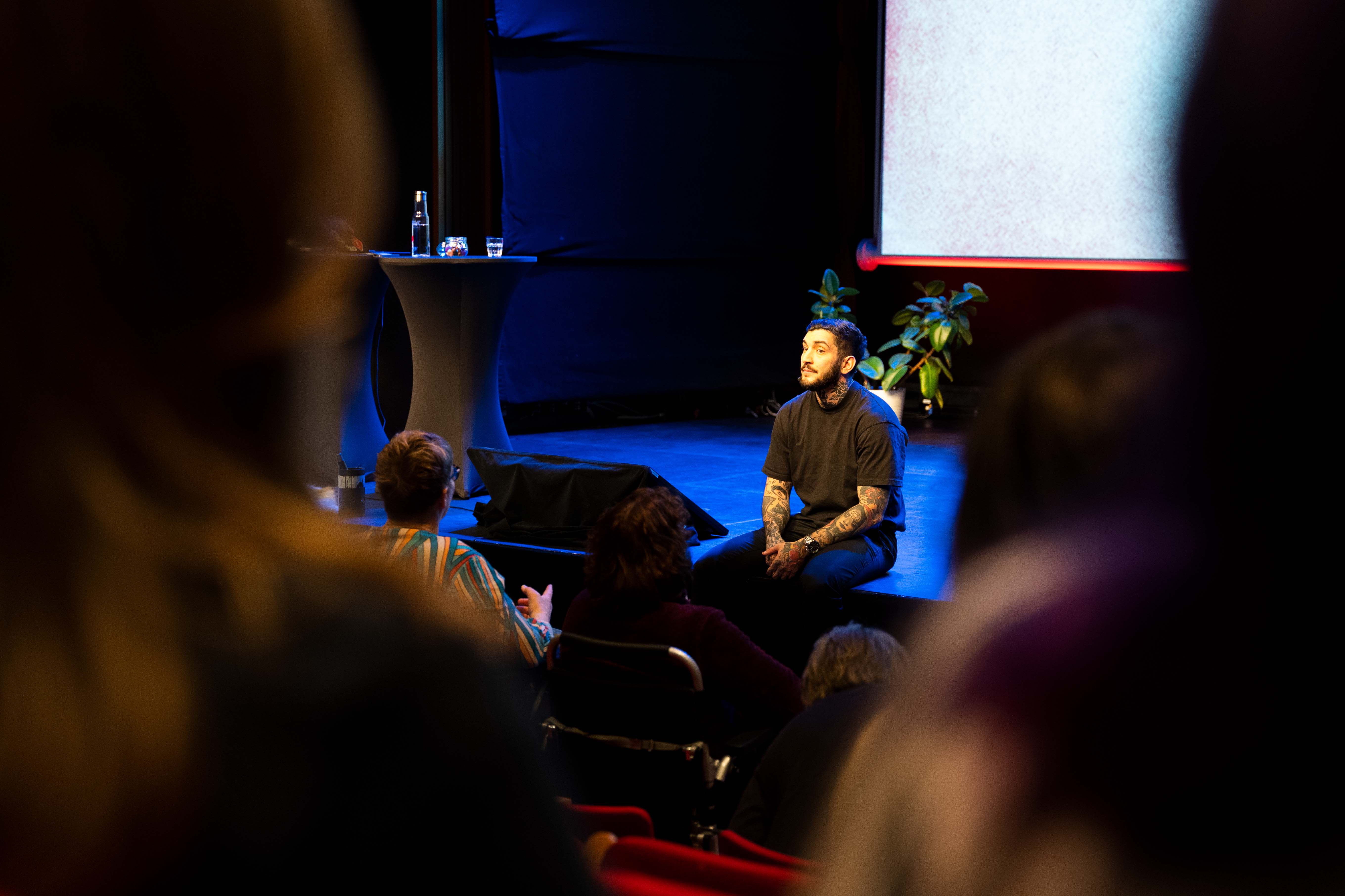 Atilla Yoldas sitter på en scenkant och pratar med publiken.