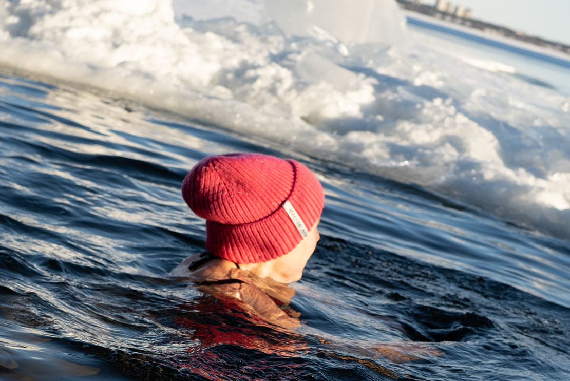 En människa med mössa på som simmar i en isvak.
