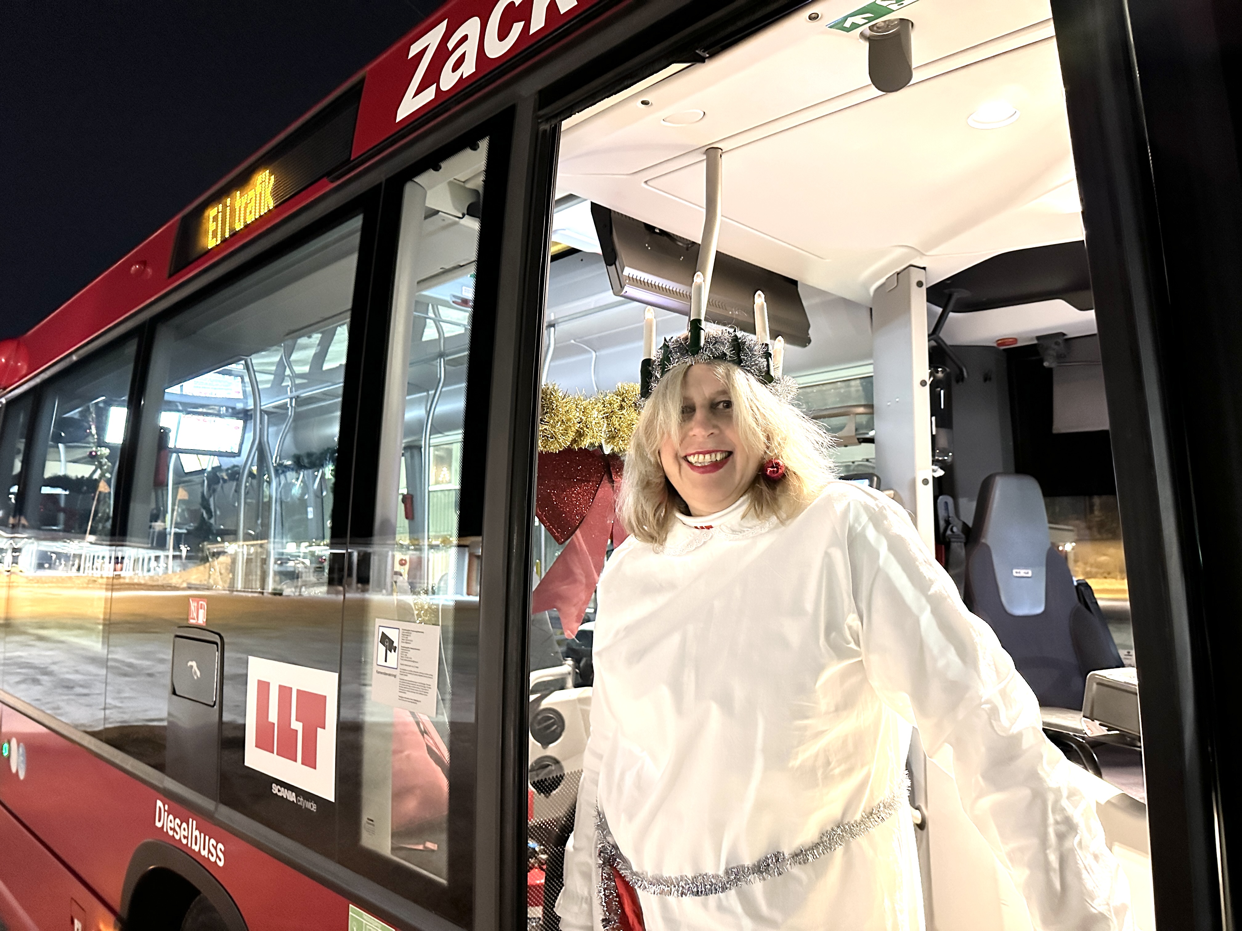 En luciaklädd bussförare står och kikar ut ur en LLT-buss.