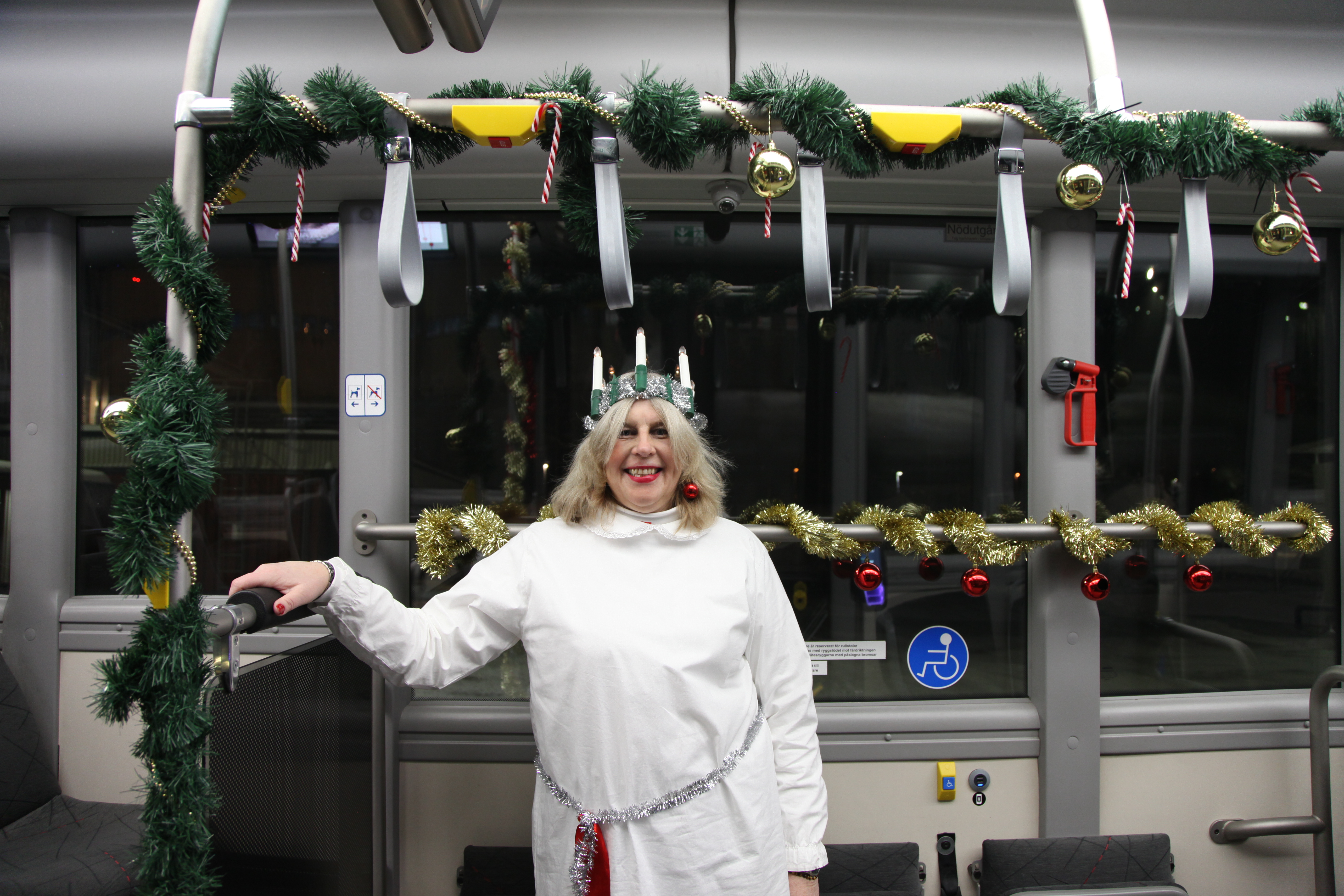 En luciaklädd busschaufför står i en julpyntad buss.