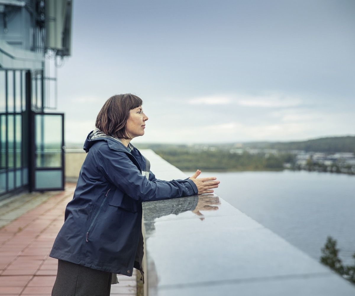 En kvinna i mörkt hår står på en terass med utsikt över staden.