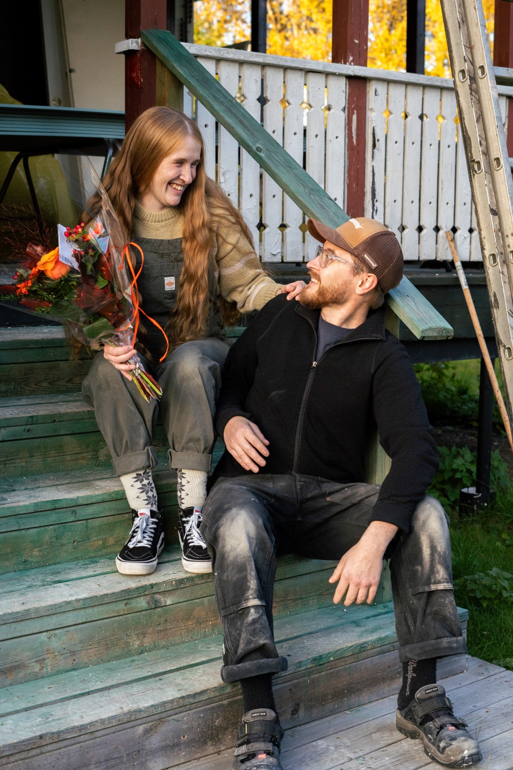 Ett par, en kvinna och en man, sitter i en trappa framför ett hus.