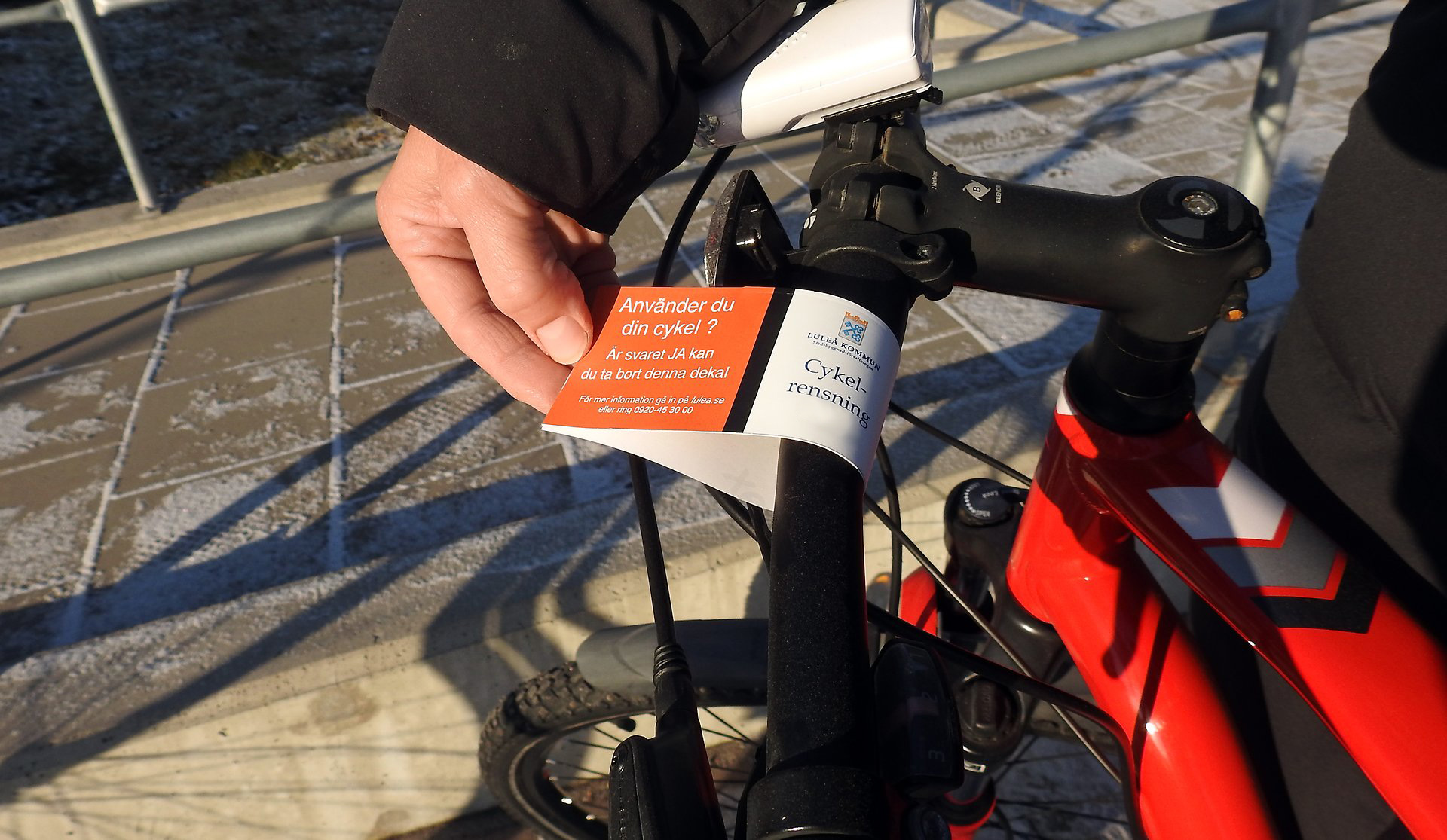 Bilden föreställer en cyckelstyre med en lapp som anger att den ska flyttas. Det syns en hand som håller i lappen.