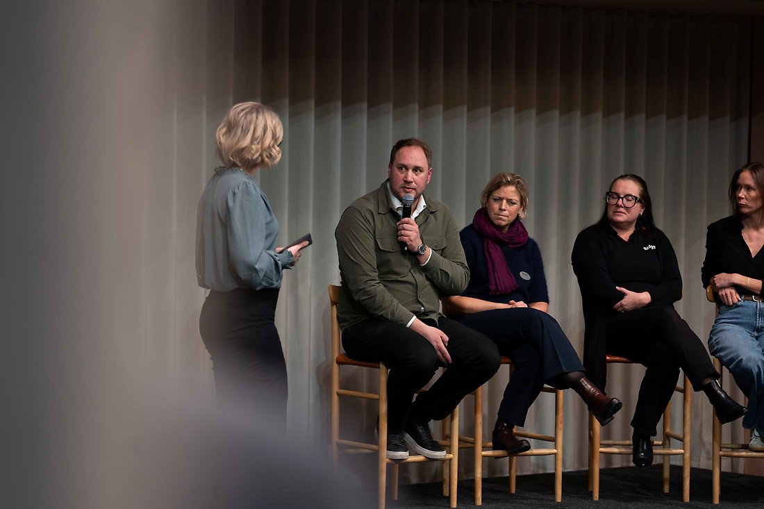 en man pratar i mikrofon, flera personer bredvid 