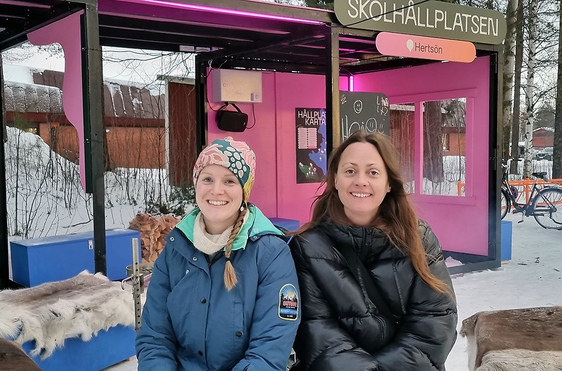 Jessica Rhodin och Ida Lemoine sitter på renskinn framför skolhållplatsen. I bakgrunden brinner en eld.