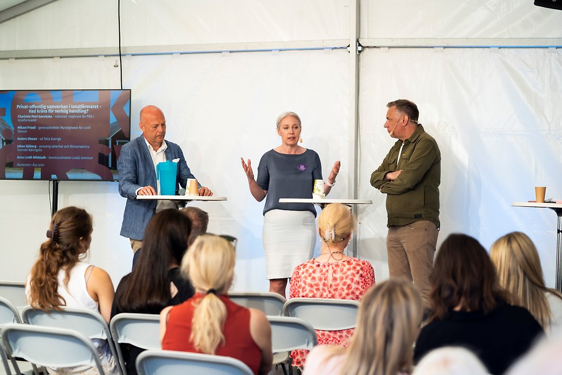 Tre personer står på en scen och pratar.